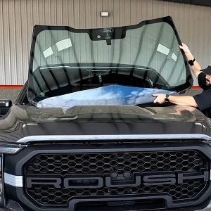 Technician positioning a replacement windshield on a pickup truck
